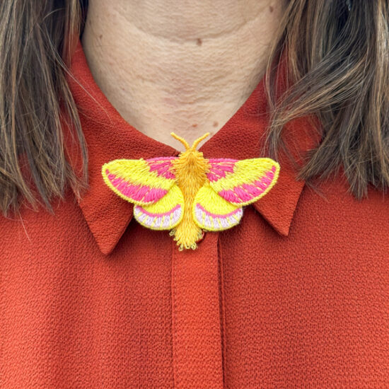 Rosy Maple moth embroidered brooch on red blouse
