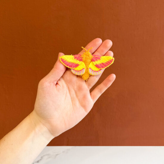 Rosy Maple moth embroidered brooch holding in hand